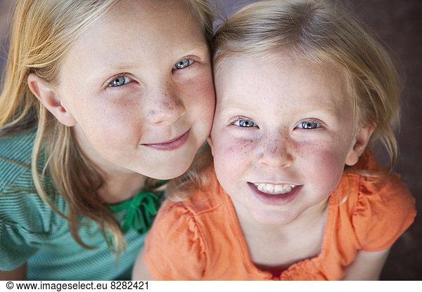 A Portrait Of Two Sisters Smiling. Two Young Girls  With Blue Eyes And Blonde Hair.
