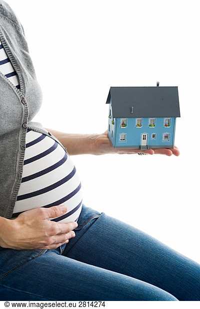 A pregnant woman holding a miniature house.