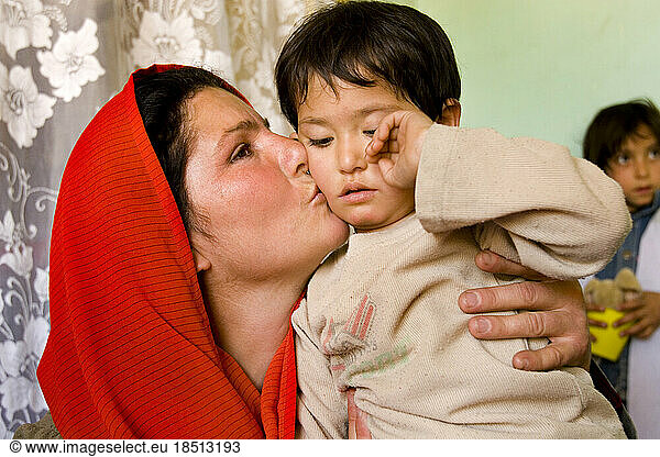 A preschool teacher in Kabul comforts a crying child with a hug and a kiss.