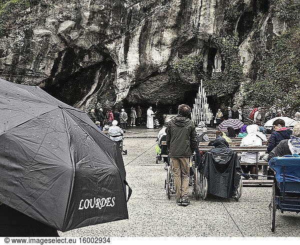 A priest recites prayers at the entrance to the Massabielle grotto of the Sanctuary of Our Lady of Lourdes  while the faithful queue to enter. It was in the grotto that Bernadette Soubirous saw apparitions of the Virgin Mary. Lourdes  Hautes-Pyr?n?es department  Occitanie  France.