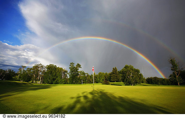 A rainbow in the sky above a golf green.
