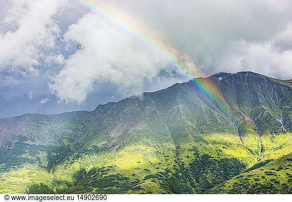 A rainbow shines through atmospheric light  lush green mountainsides in the background  Hatcher Pass  South-central Alaska; Palmer  Alaska  United States of America