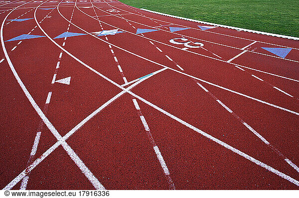 A red artificial surface running track. A sports ground. Painted marked lines for lanes.