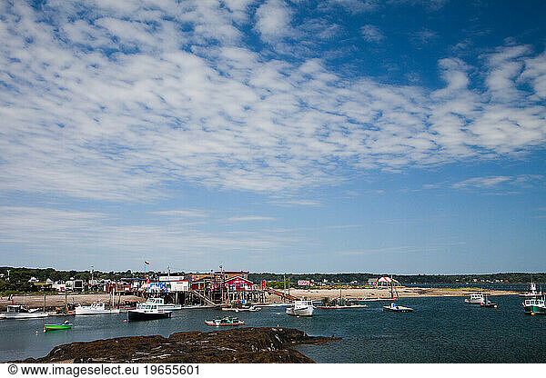 A red building on the edge of a small harbor with boats floating on a sunny day.