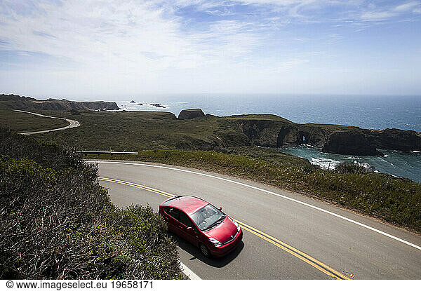 A red car drives on a highway near the ocean.
