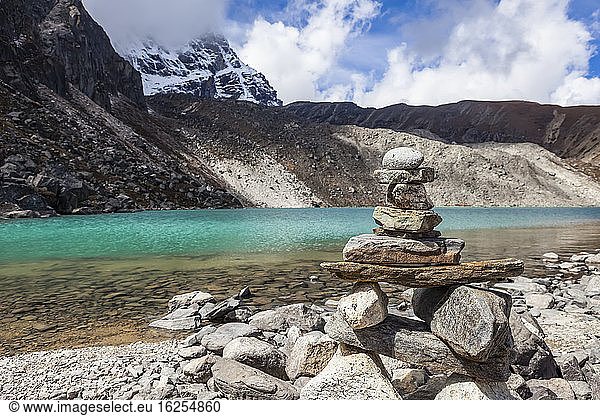 A rock cairn sits in front of one of the turquoise coloured sacred lakes in the Gokyo region  on a crisp  sunny autumn day  with fresh snow on the Himalayan mountains in the background in Sagarmatha National Park  Solukhumbu District  Nepal; Solukhumbu District  Nepal