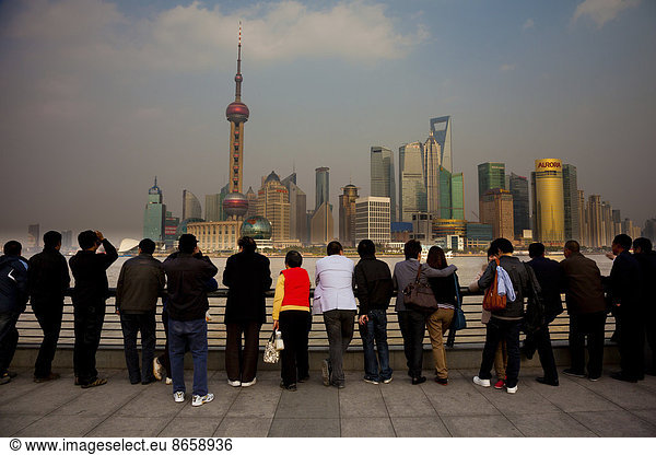 A row of people looking at the Shanghai Pudong skyline  including the Oriental Pearl Tower  the Shanghai World Financial Center and the Jin Mao Tower  viewed from over the Huangpu River