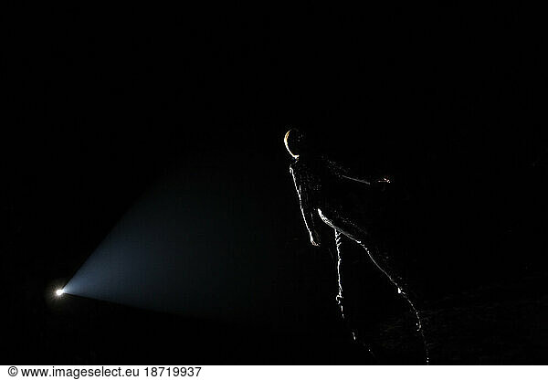 A runway fashion model walks down the catwalk  illuminated by a spotlight.