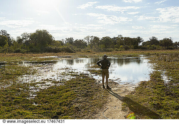 A safari guide on foot by a water pool  surveying the terrain.
