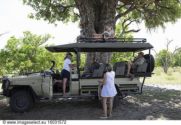 A safari jeep parked in the shade with six family members resting.
