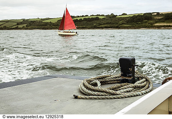 A sailing boat with bright red sails on the water  seen from another boat.