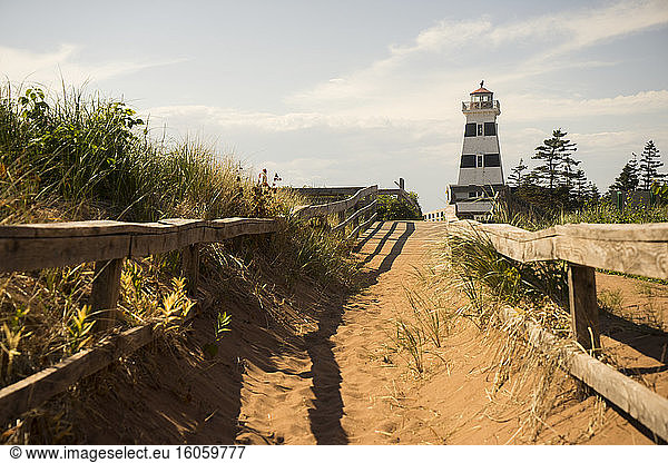 A sandy trail and wooden rail fence leading to a lighthouse on the coast; Prince Edward Island  Canada