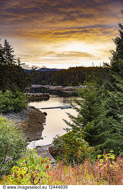 A scenic view of the coastline with forests and foliage in autumn colours and a small boat moored along a dock near Tutka Bay  on the southern end of Kachemak Bay; Homer  Alaska  United States of America