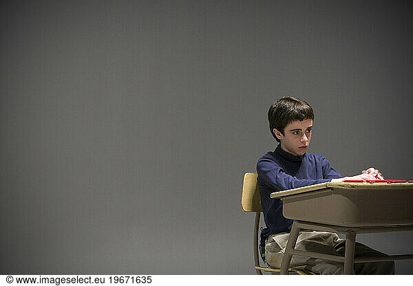 A school boy sitting at a desk in empty room.