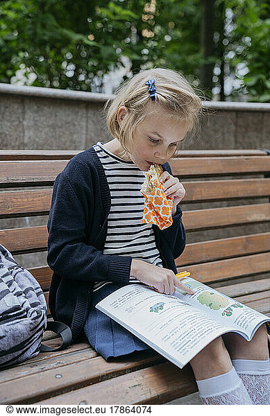 A schoolgirl eats a sandwich in the park and does her homework.