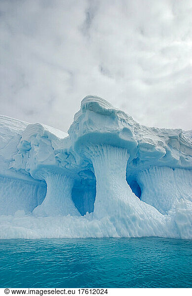 A sculpted iceberg under a fully clouded sky.