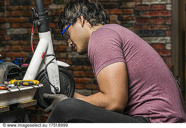 A seated mechanic puts a wheel of an electric scooter back in place