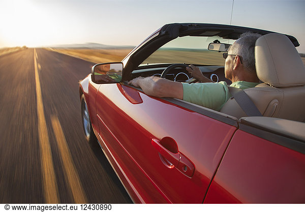 A senior Hispanic man at the wheel of his convertible sports car at sunset in eastern Washington State  USA.