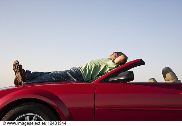 A senior male relaxing on the hood of his convertible sport car.