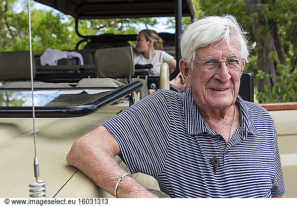 A senior man standing by a safari jeep smiling.