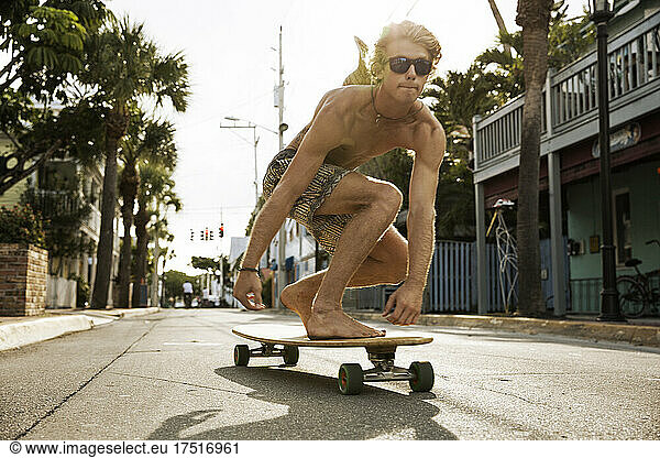 A shirtless young man skates down the middle of the road in the keys