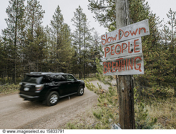 a sign on a dirt road with speeding car warning drivers to slow down