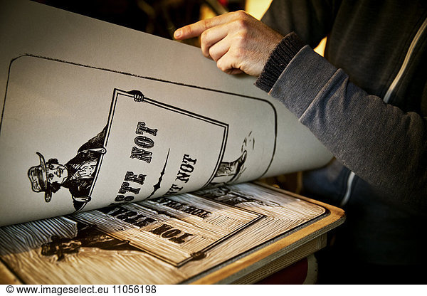 A sign writer lifting a sheet of imprinted card off a cut-out linoleum surface  a woodcut.
