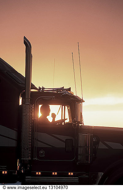 A silhouette of a truck driver on his CB radio in the cab of his Class 8 truck.
