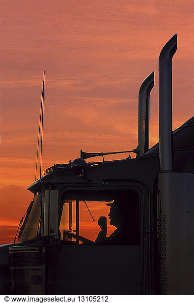 A silhouette of a truck driver on his CB radio in the cab of his Class 8 truck tractor.