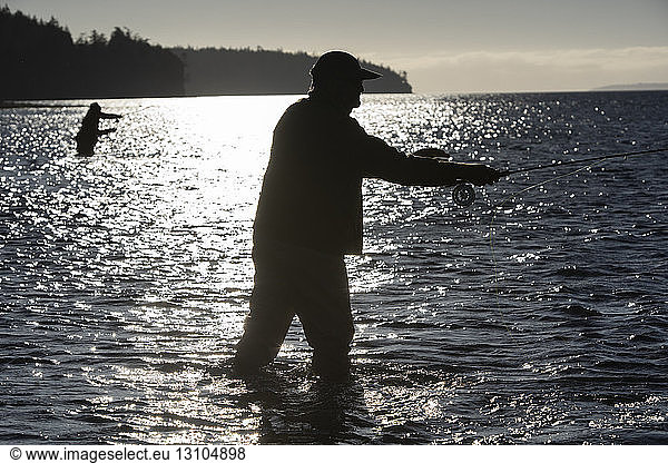 A silhouette of two fly fishermen standing in salt water while fly fishing for searun coastal cutthroat trout and salmon in northwest Washington State USA