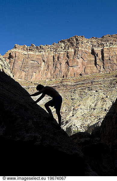 A silhouetted man scrambles up a rock wall in Eardley Canyon  San Rafael Swell  Utah.