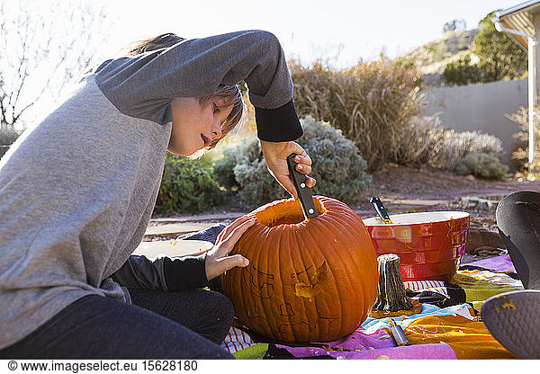 A six year old boy carving a pumpkin at Halloween.