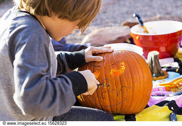 A six year old boy carving pumpkin outdoors at Halloween.