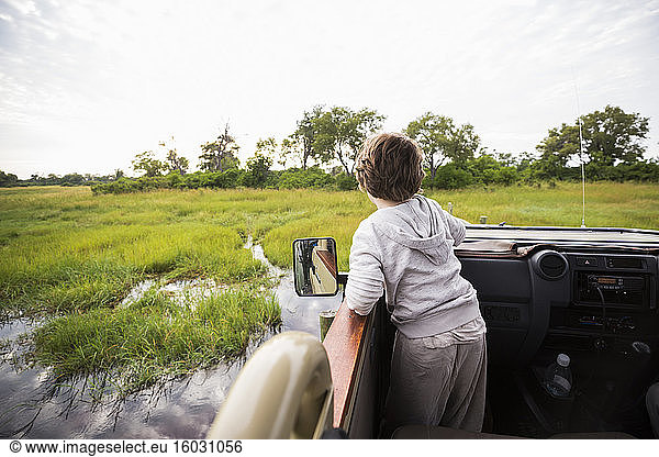 A six year old boy in a safari jeep driving through water in marshes.