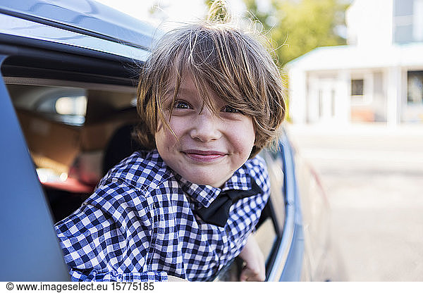 A six year old boy smiling at camera  looking out of car window