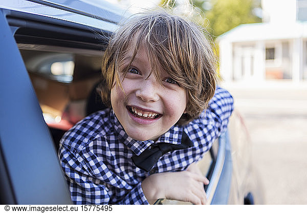 A six year old boy smiling at camera  looking out of car window