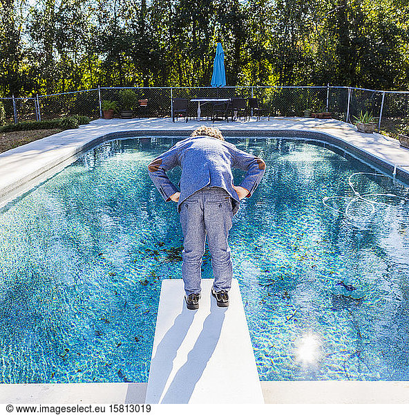 A six year old boy standing on diving board overlooking pool