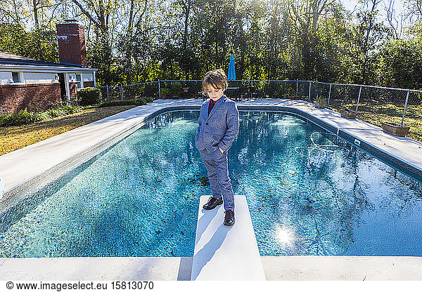 A six year old boy standing on diving board overlooking pool