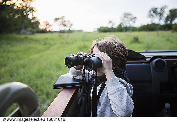 A six year old boy using binoculars seated in a safari jeep.