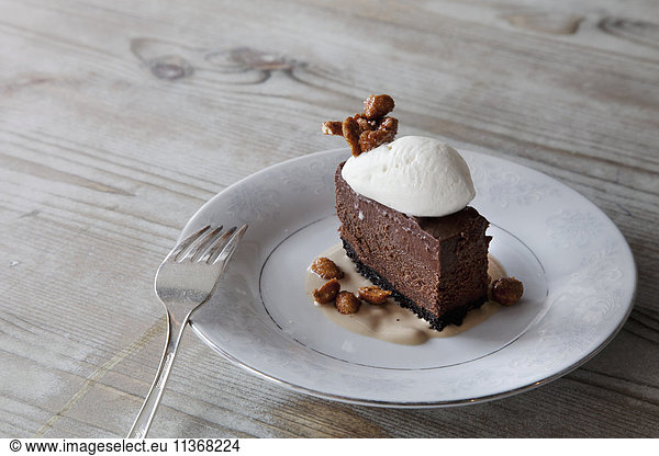 A slice of chocolate mousse dessert with ice cream  nuts and sauce on a plate.