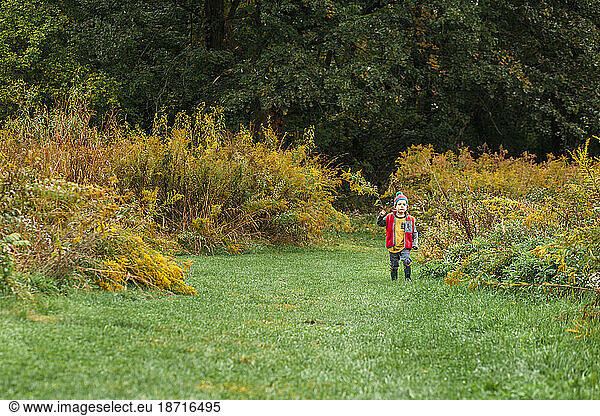 A small child in a knit cap walks alone in field of tall yellow grass