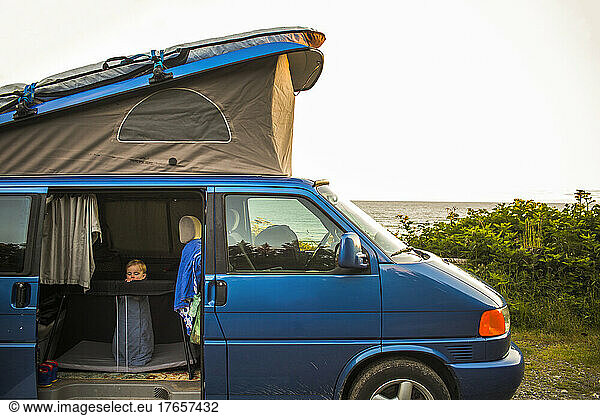 A small child in a pack-n-play inside a pop-top camper van by beach