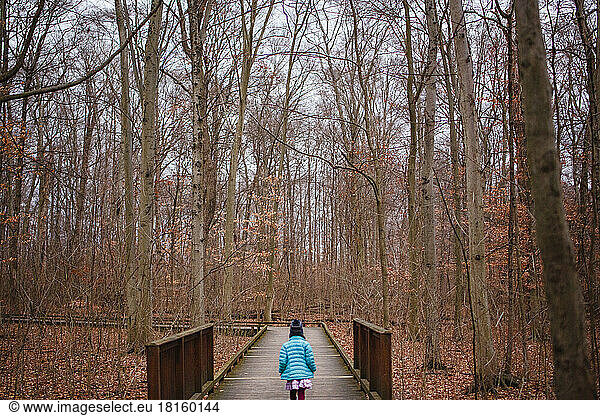 A small child in colorful jacket walks alone on a wooded path at dusk
