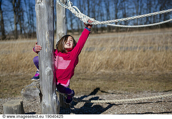 A small child reaches to pull herself up on a rope balance beam