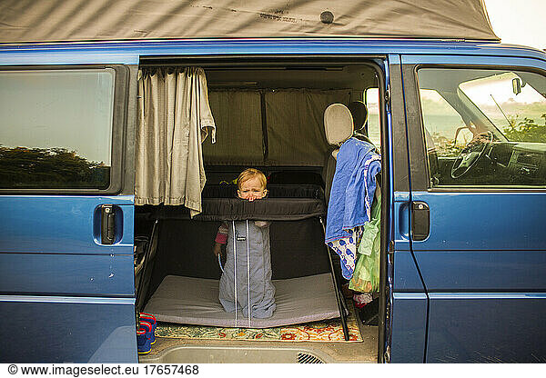 A small child stands in a crib inside a camper van