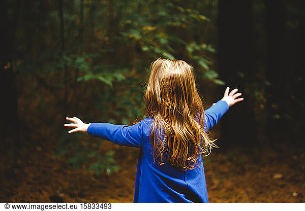 A small girl throws out arms to embrace the dark woods in front of her