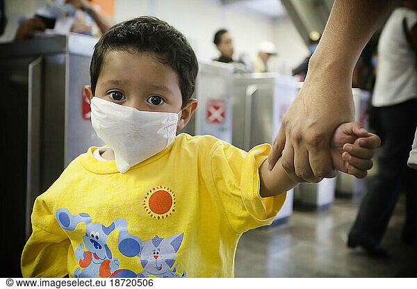 A small kid wearing a mask is held by his mother's hand at a metro station in Mexico City  DF  Mexico.