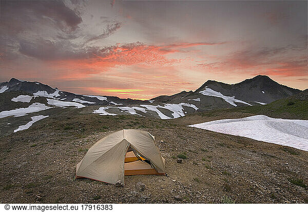 A small tent pitched on a screen slope just below the snowline  at sunset in the Mount Baker wilderness.