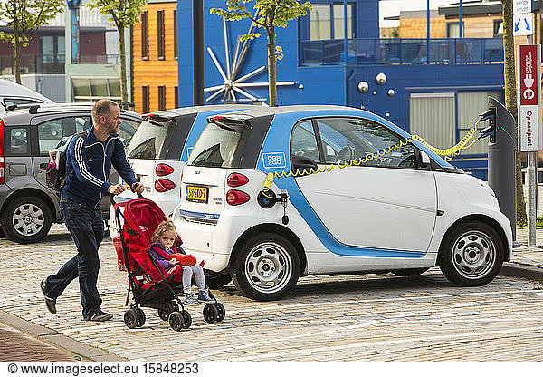 A Smart car electric car at a charging station for electric cars in Ijburg  Amsterdam  Netherlands  in front of floating houses.
