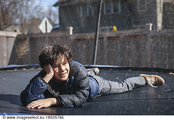 A smiling boy lays on a trampoline outside in winter